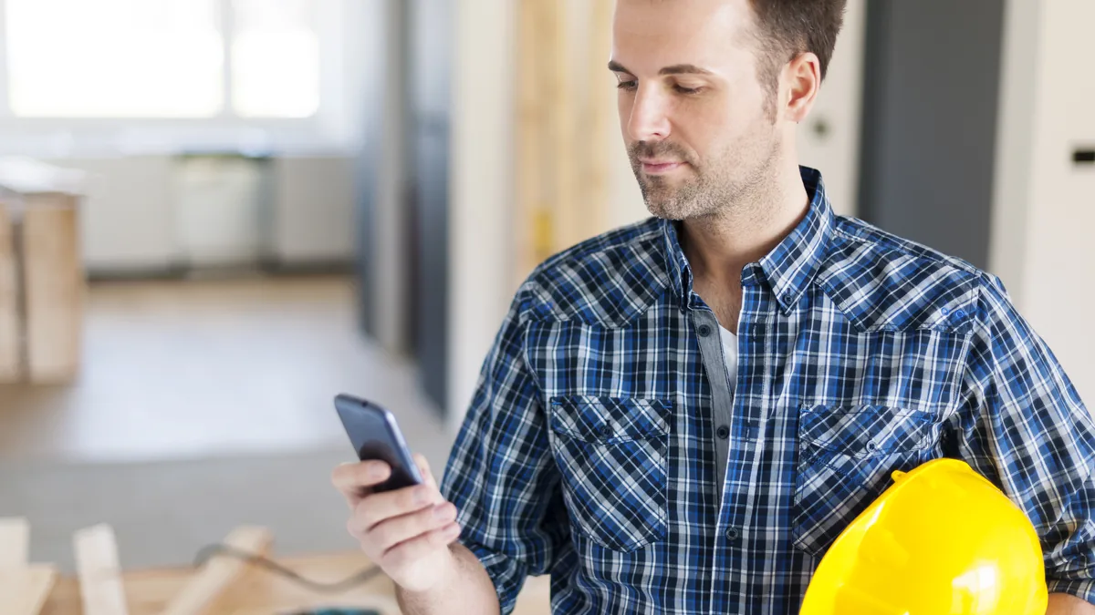 Contractor reading a smartphone message inside a home under renovation.