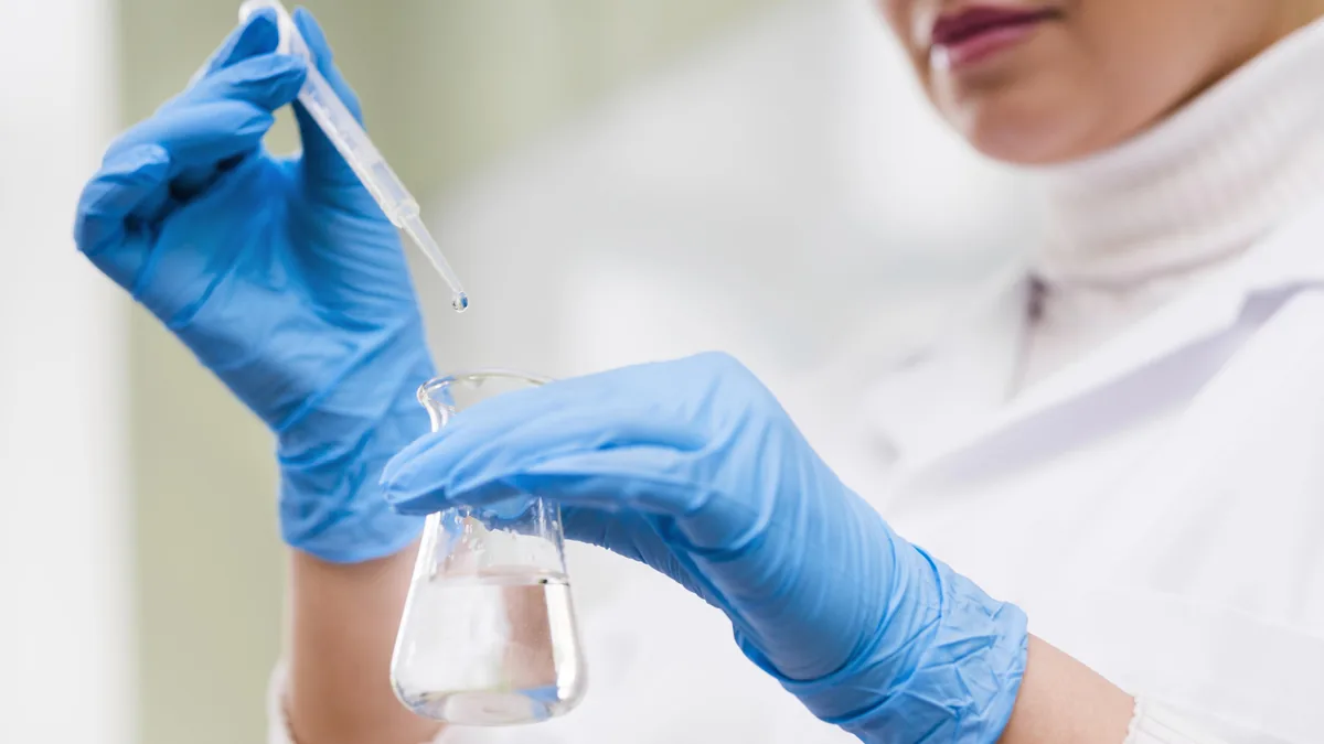 Gloved hands using a pipette with laboratory glassware.