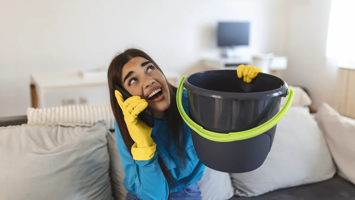Homeowner making a phone call while collecting water from a ceiling leak.