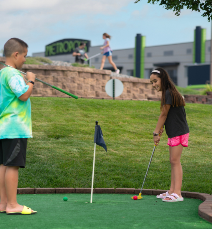 Young siblings playing mini golf on the outdoor mini golf course at Action City in Eau Claire, WI. Young siblings playing mini golf on the outdoor mini golf course at Action City in Eau Claire, WI.