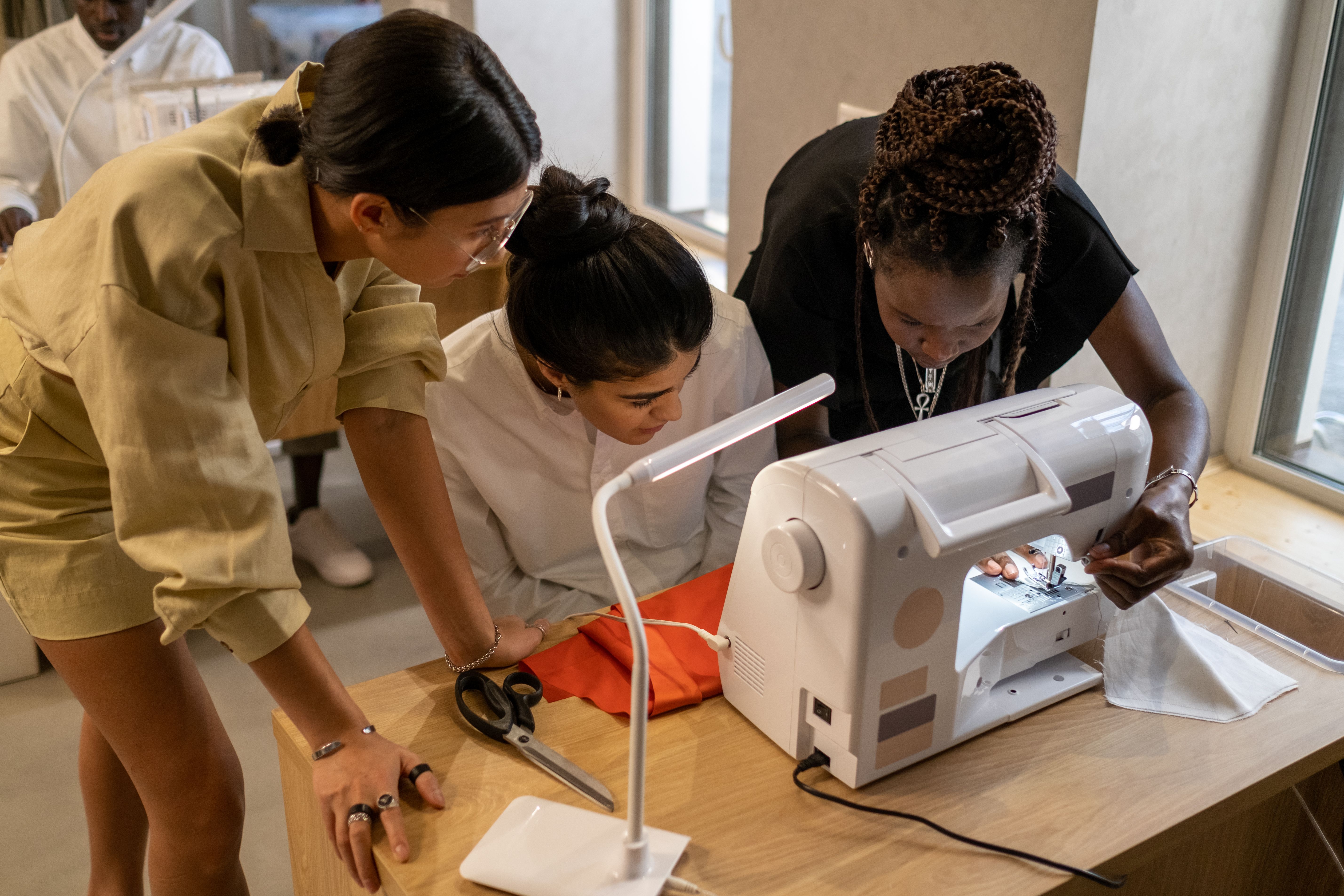 Apparel professionals working together around a single sewing machine, illustrating the manual-coordination model that compliance infrastructure eventually replaces. Apparel professionals working together around a single sewing machine, illustrating the manual-coordination model that compliance infrastructure eventually replaces.