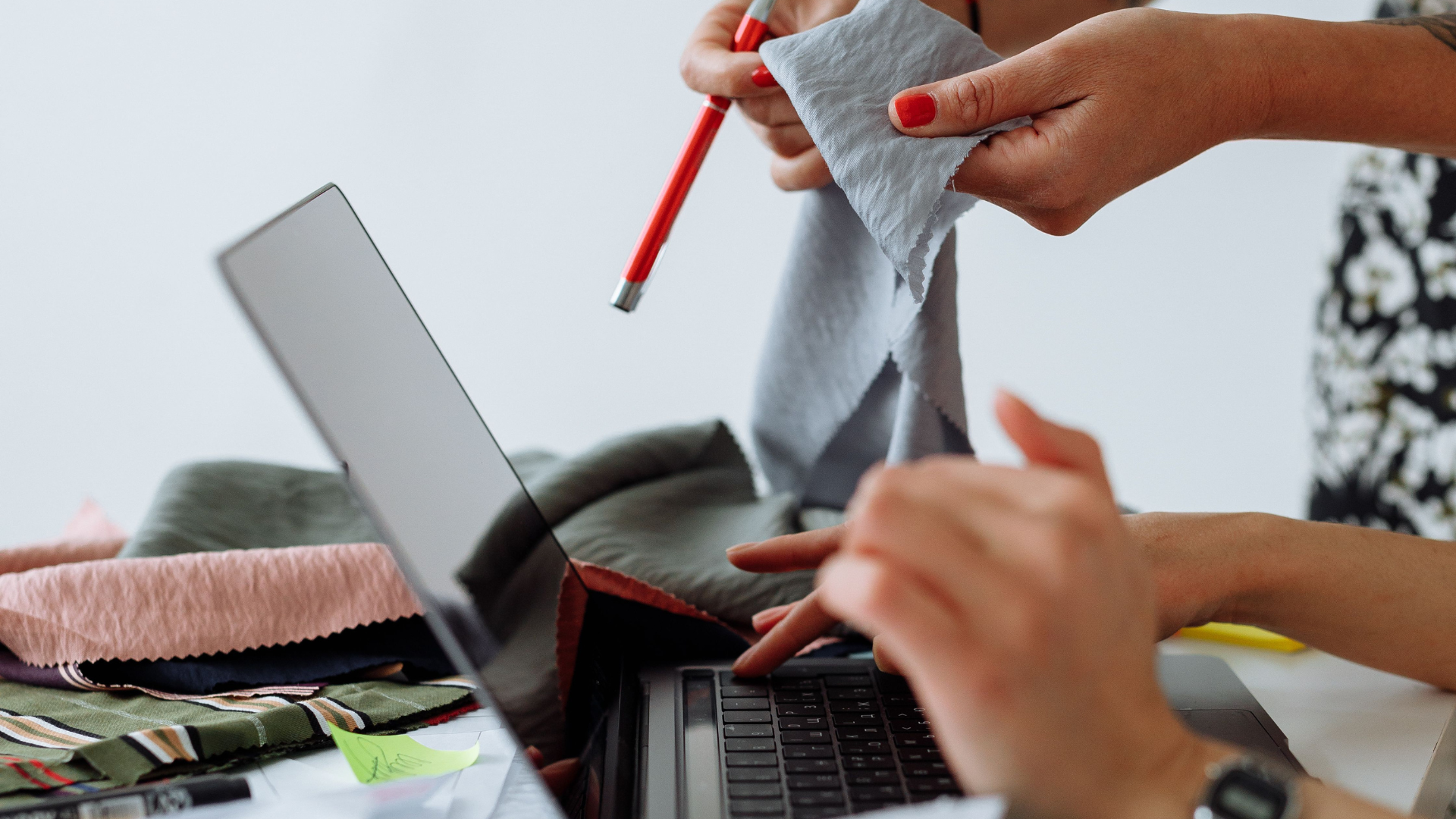 Two apparel professionals reviewing fabric swatches at a laptop, illustrating the catalog audit and product classification work required for SB 707 readiness.