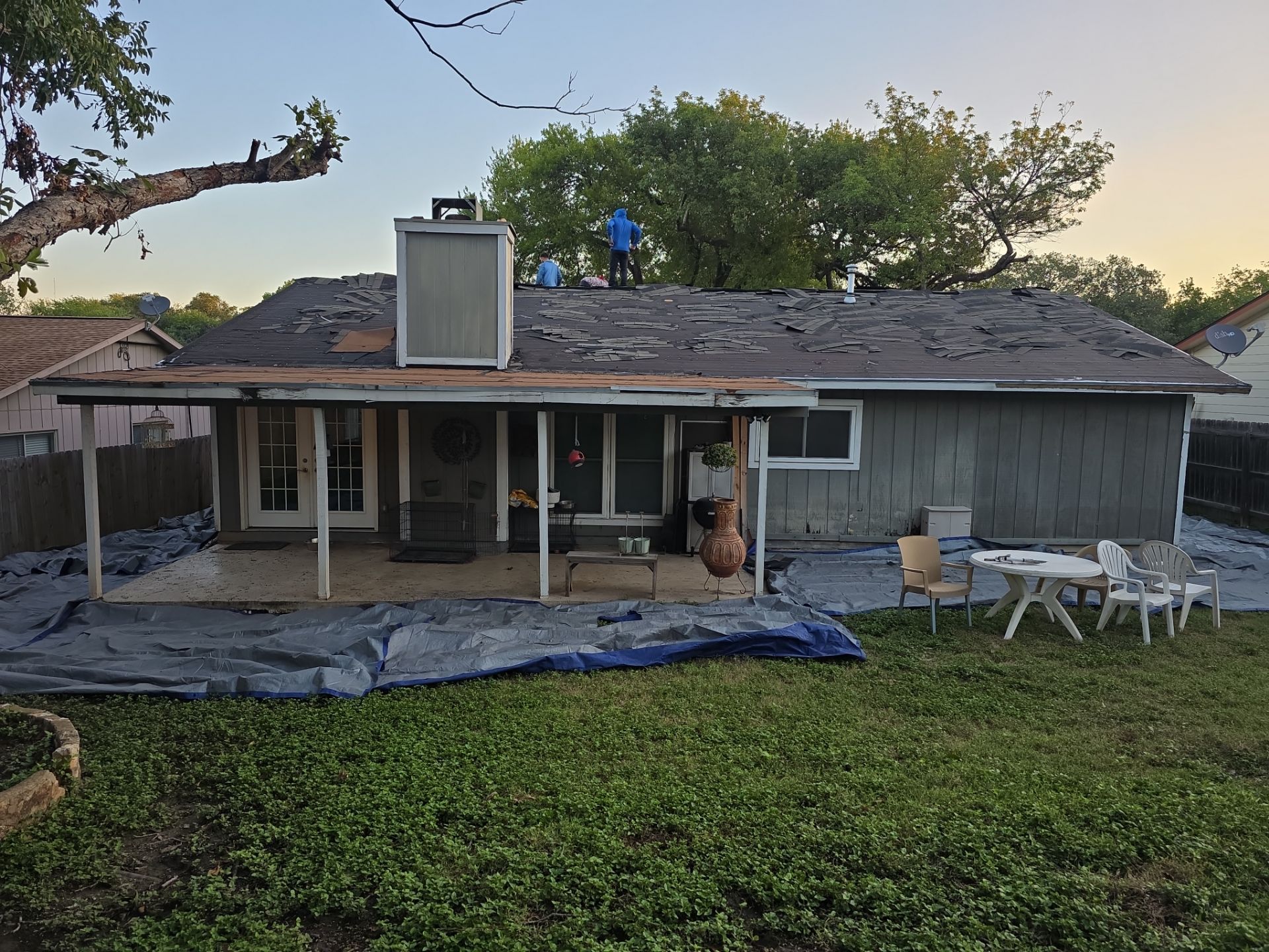 Rear exterior view of Lake Champlain San Antonio residence with roofing workers on roof and protective tarps during restoration