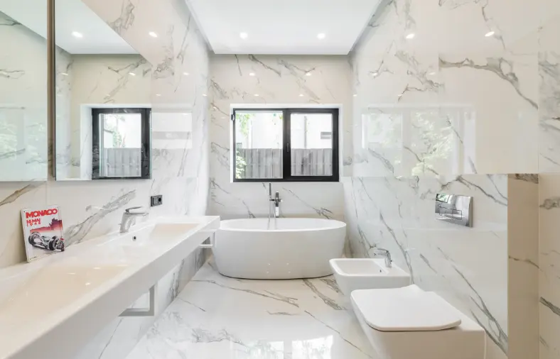 Renovated bathroom with white dual sink, marble tiles, island bathtub and toilet .