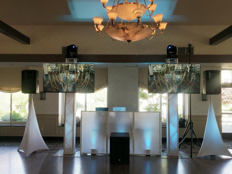 Two screens on truss beside a white DJ booth in a ballroom
