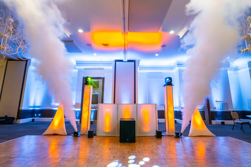 CO2 cannons firing columns of cold fog beside a DJ booth with uplit spandex stands