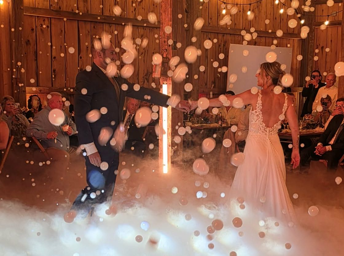 Couple sharing their first dance on a cloud of low fog with falling bubbles