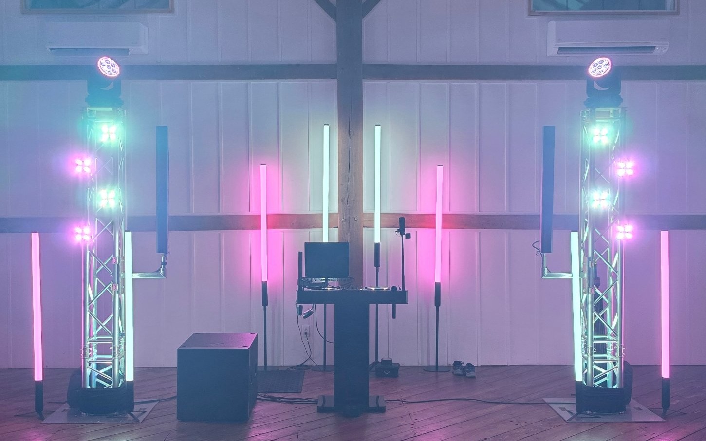 DJ setup with pink and green lighting and two moving head lights on truss