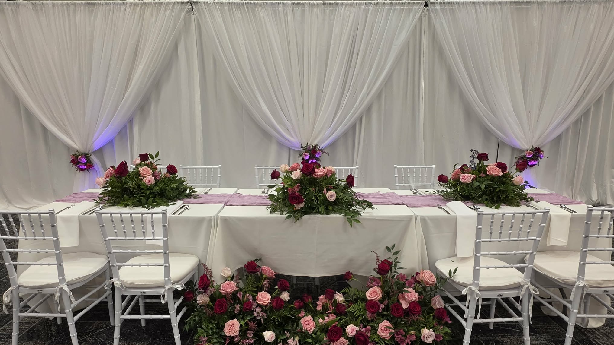 Head table framed by white pipe and drape with uplighting