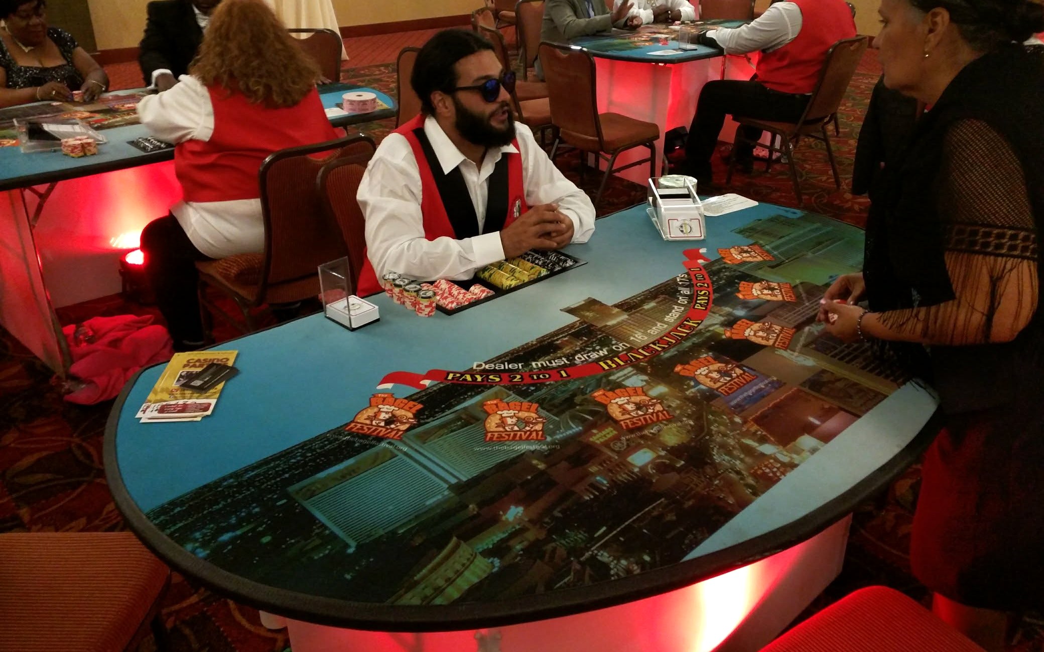 Blackjack table with a dealer, a tray of casino-style chips and a red uplit facade at a corporate gala casino night