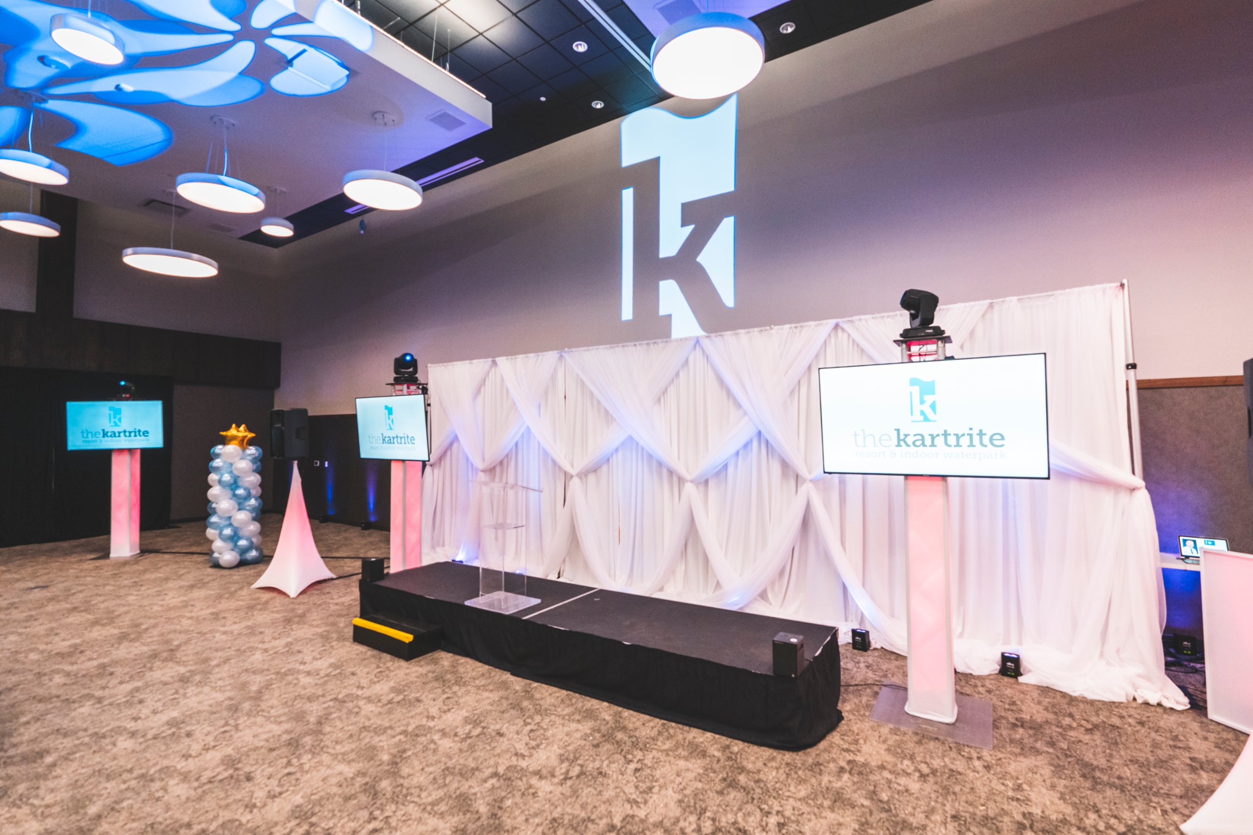 Stage with white pipe and drape, screens on truss and a projected logo at The Kartrite Resort