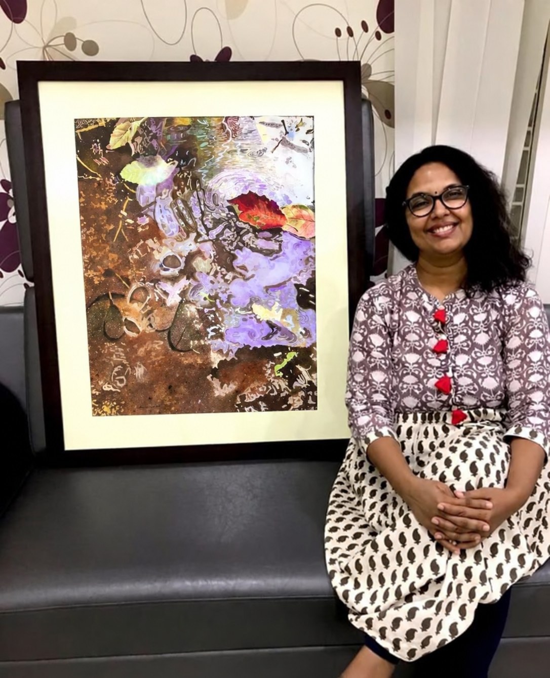 Dr. Amrita Gandhi sitting beside her framed first project painting