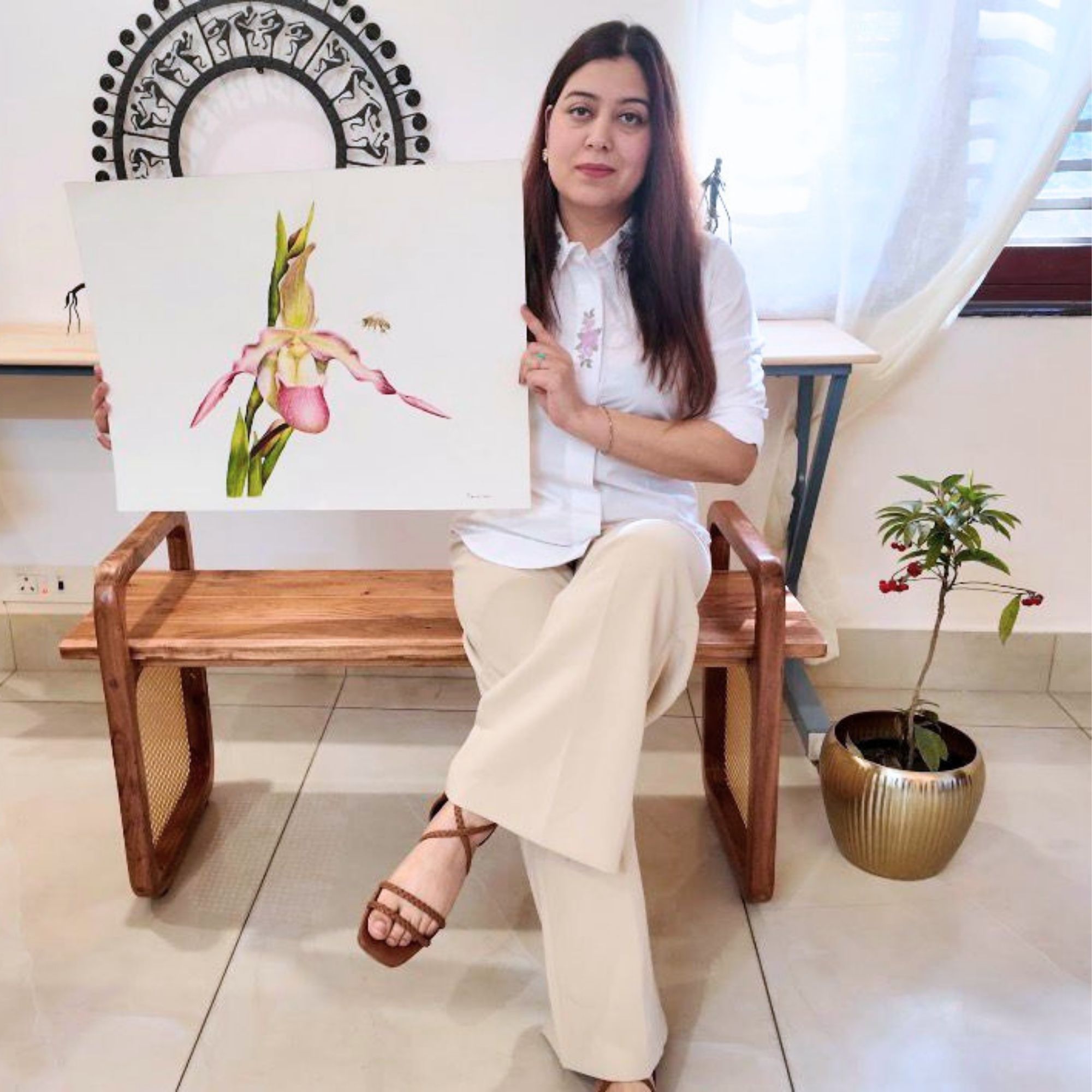 Prerna Joshi seated on a bench holding her orchid watercolor painting
