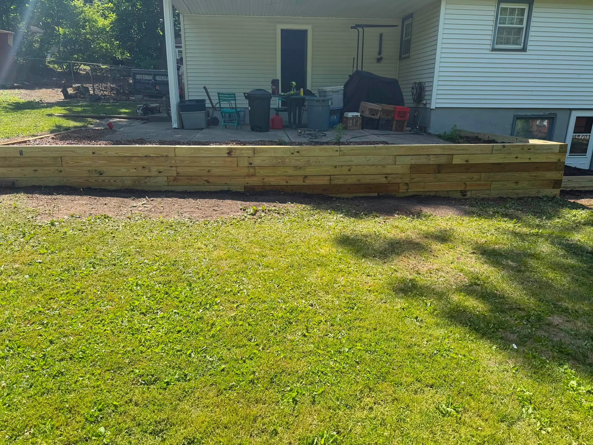 Wooden retaining wall in front of a house with a patio and outdoor furniture
