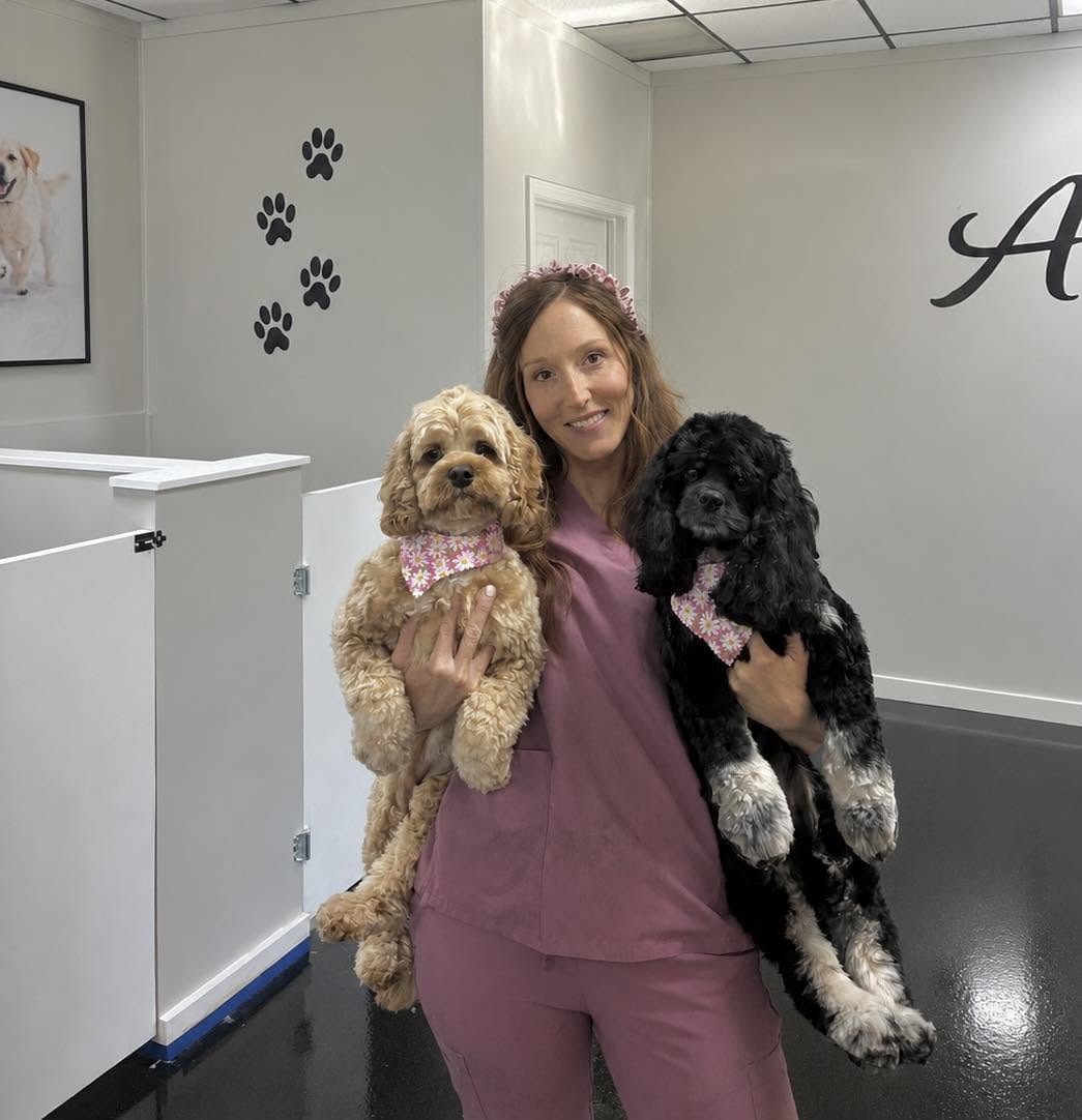 Monica holding two freshly groomed pups wearing matching daisy bandanas inside the shop