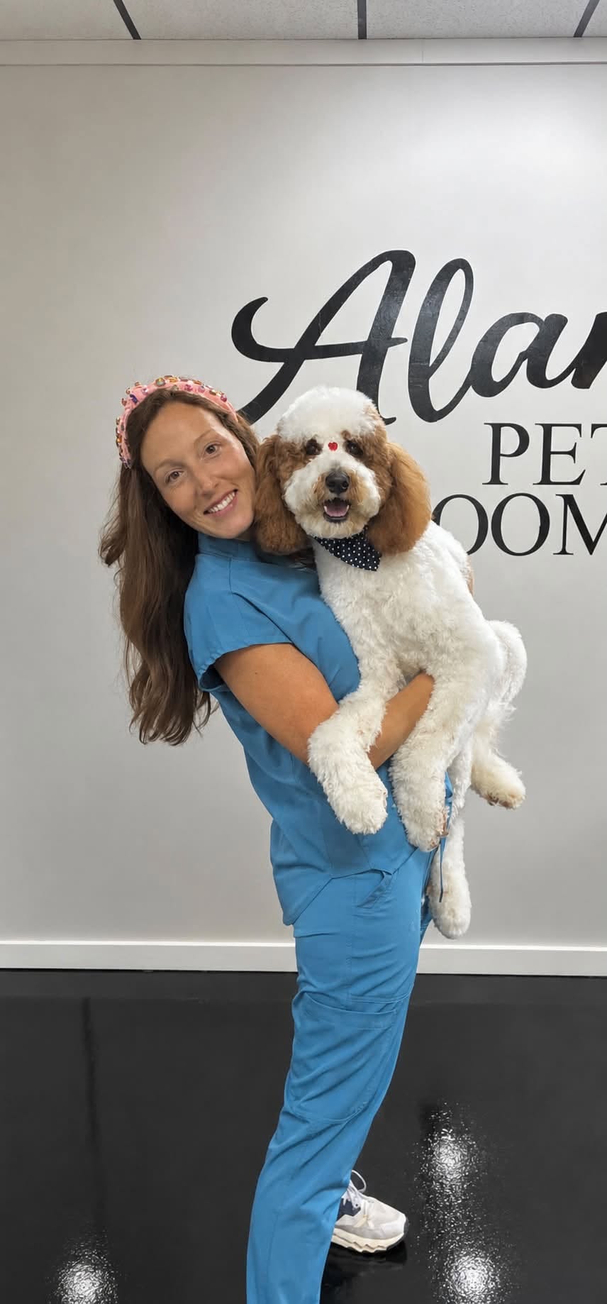 Monica holding a freshly groomed apricot-and-white poodle wearing a polka-dot bow tie