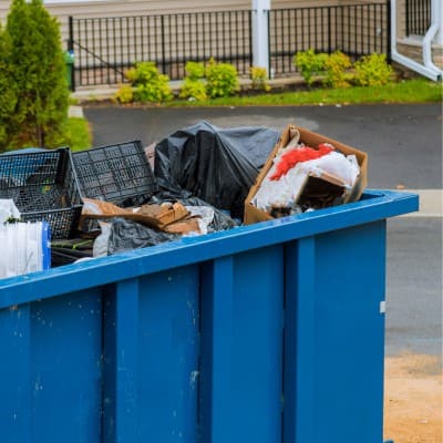 Blue dumpster filled with various trash and recyclable materials