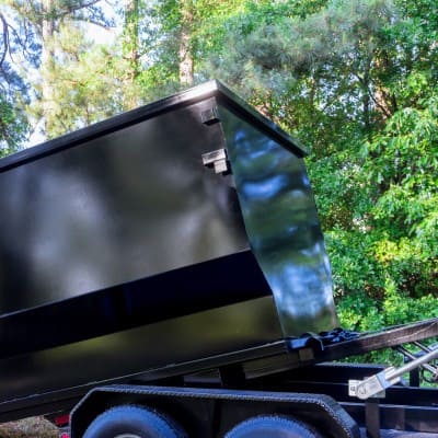 Black dumpster being loaded onto a trailer for transport