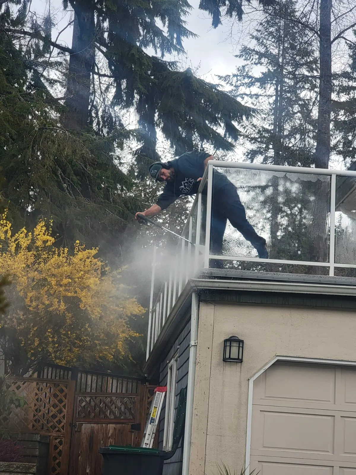Pressure washing a second-storey glass railing on a Metro Vancouver home