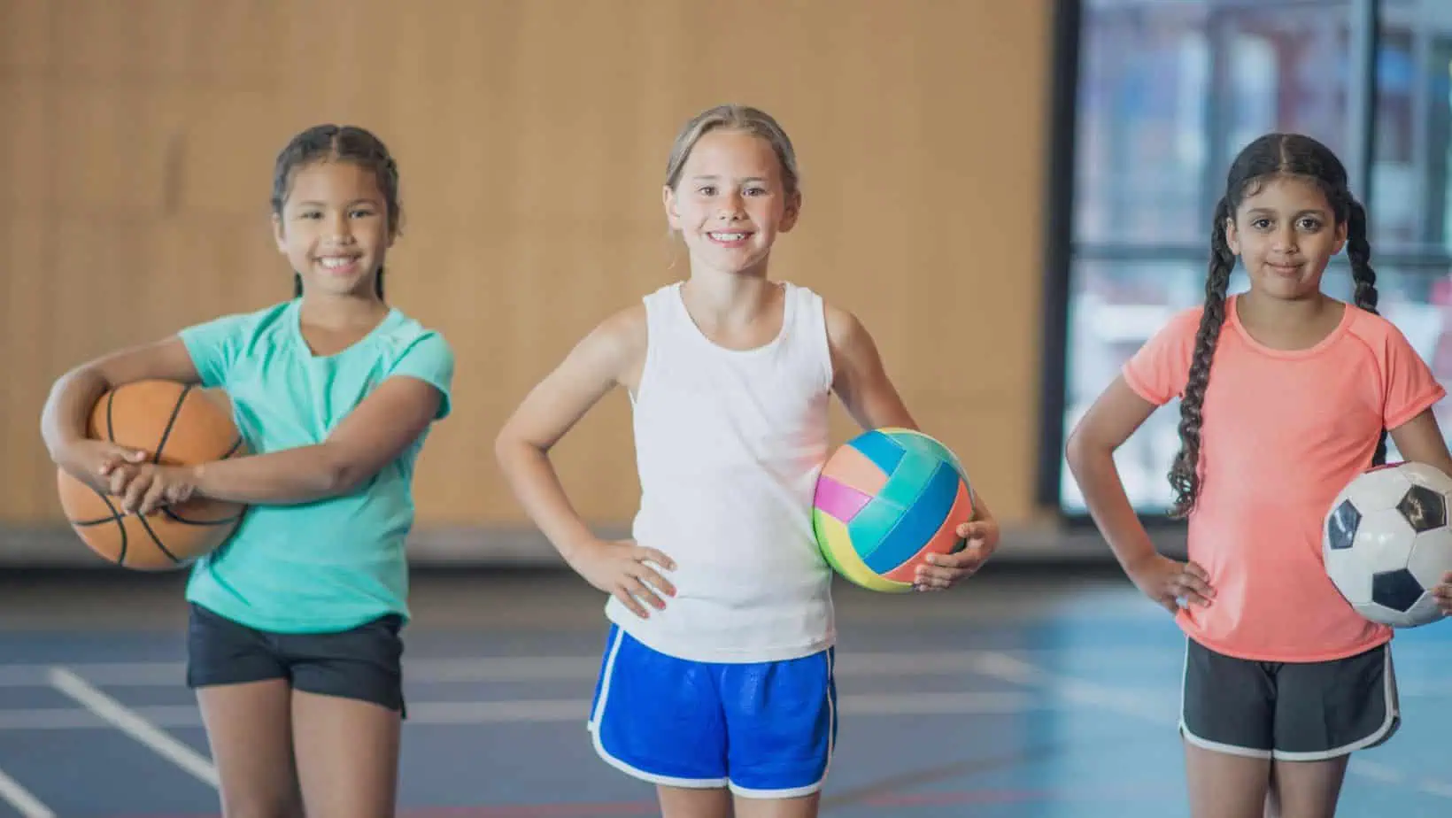 Junge Spielerinnen aus Handball, Fußball und Basketball stehen mit Bällen in der Halle