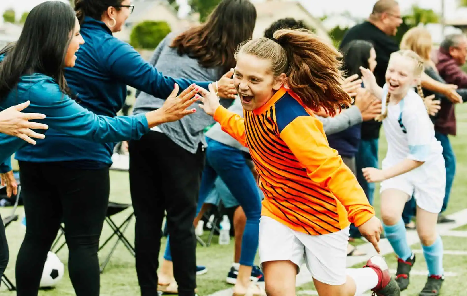 Junge Fußballerinnen klatschen Eltern ab und jubeln.