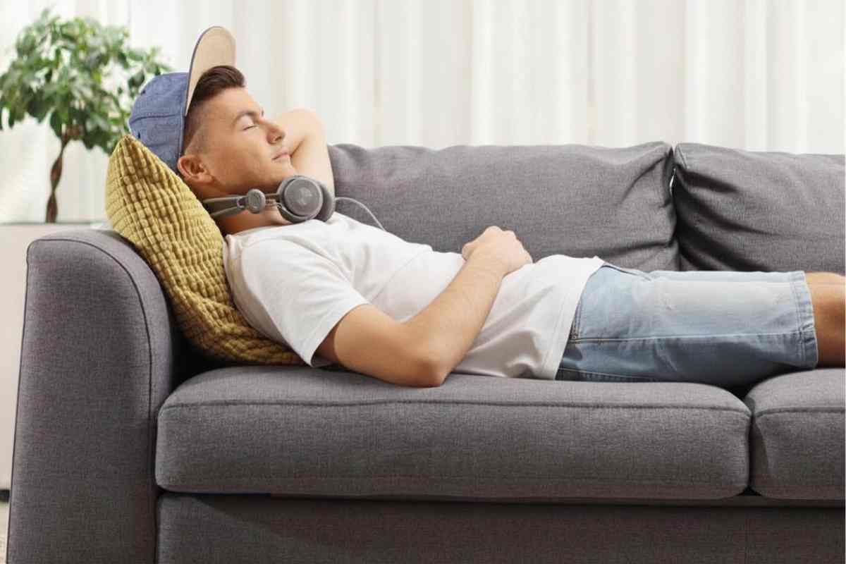 Junger Erwachsener liegt auf Sofa und macht einen Powernap