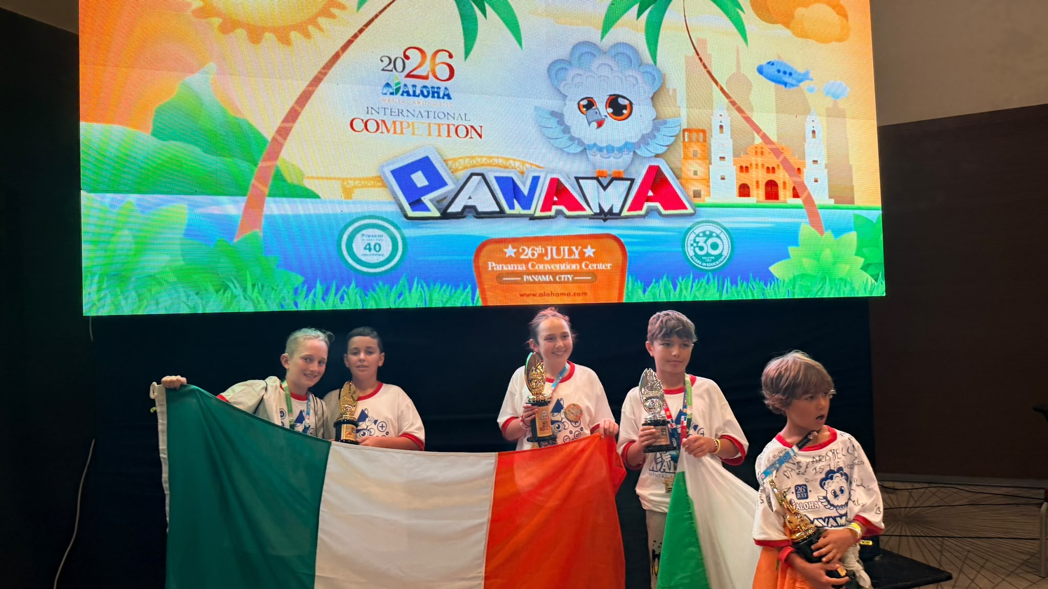 ALOHA Ireland students on stage with the Irish flag and trophies at the 2026 International Competition in Panama
