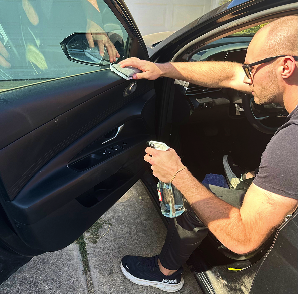  Man cleaning a car door panel with a microfiber cloth and spray bottle during interior auto detailing.