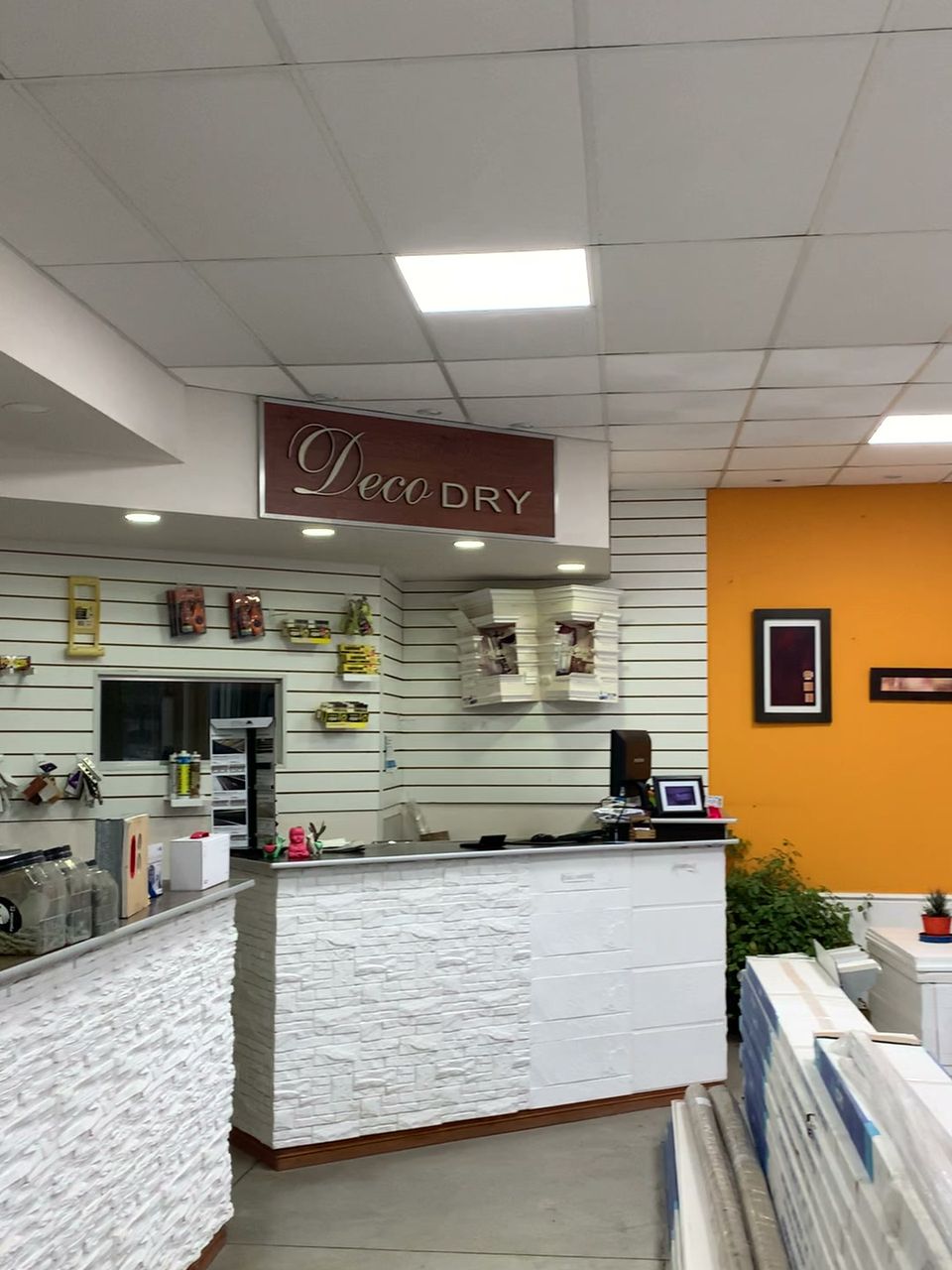 Interior del local DecoDry con mostrador revestido, pared naranja y materiales en exhibición