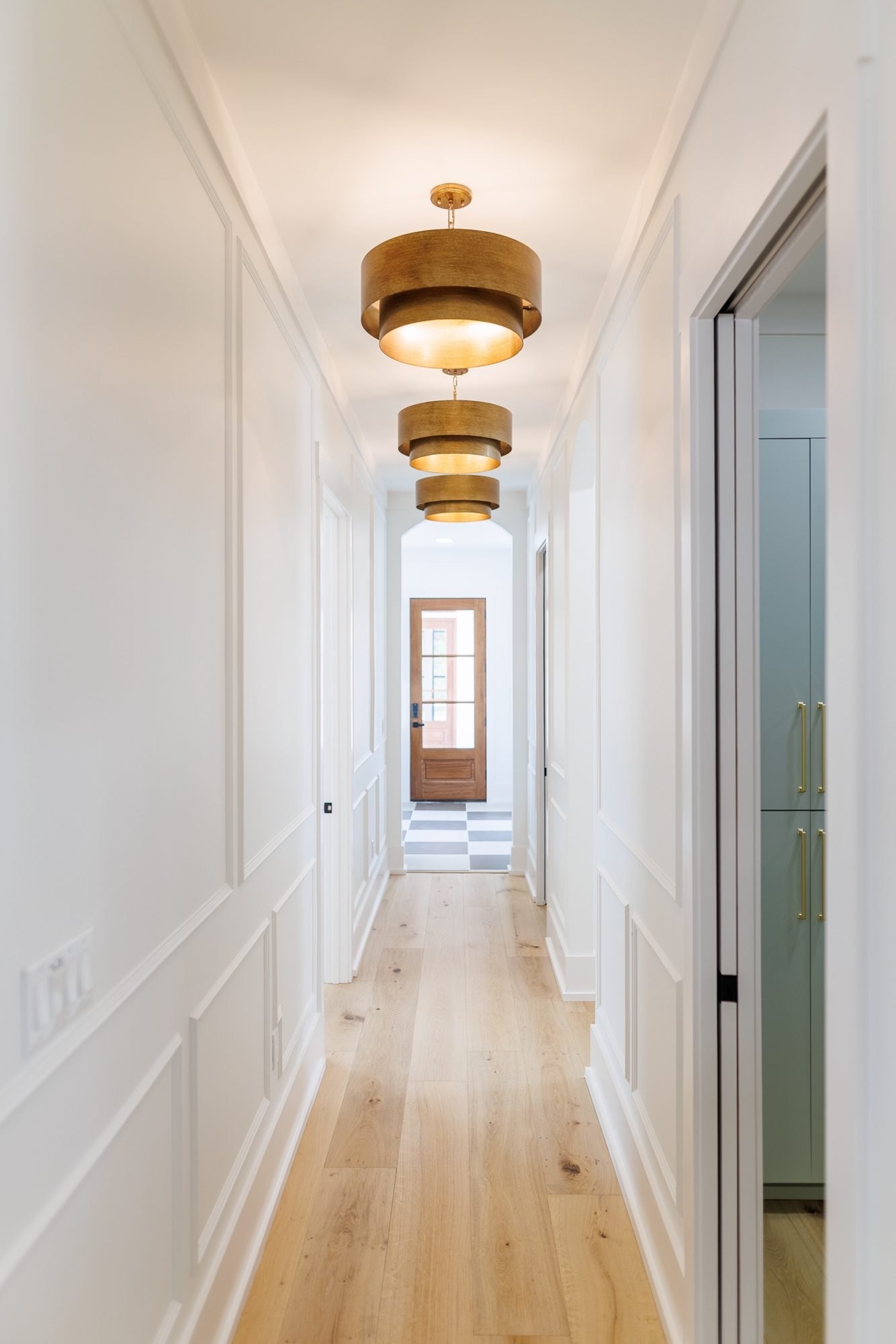 Long hallway with paneled walls and brass drum pendants