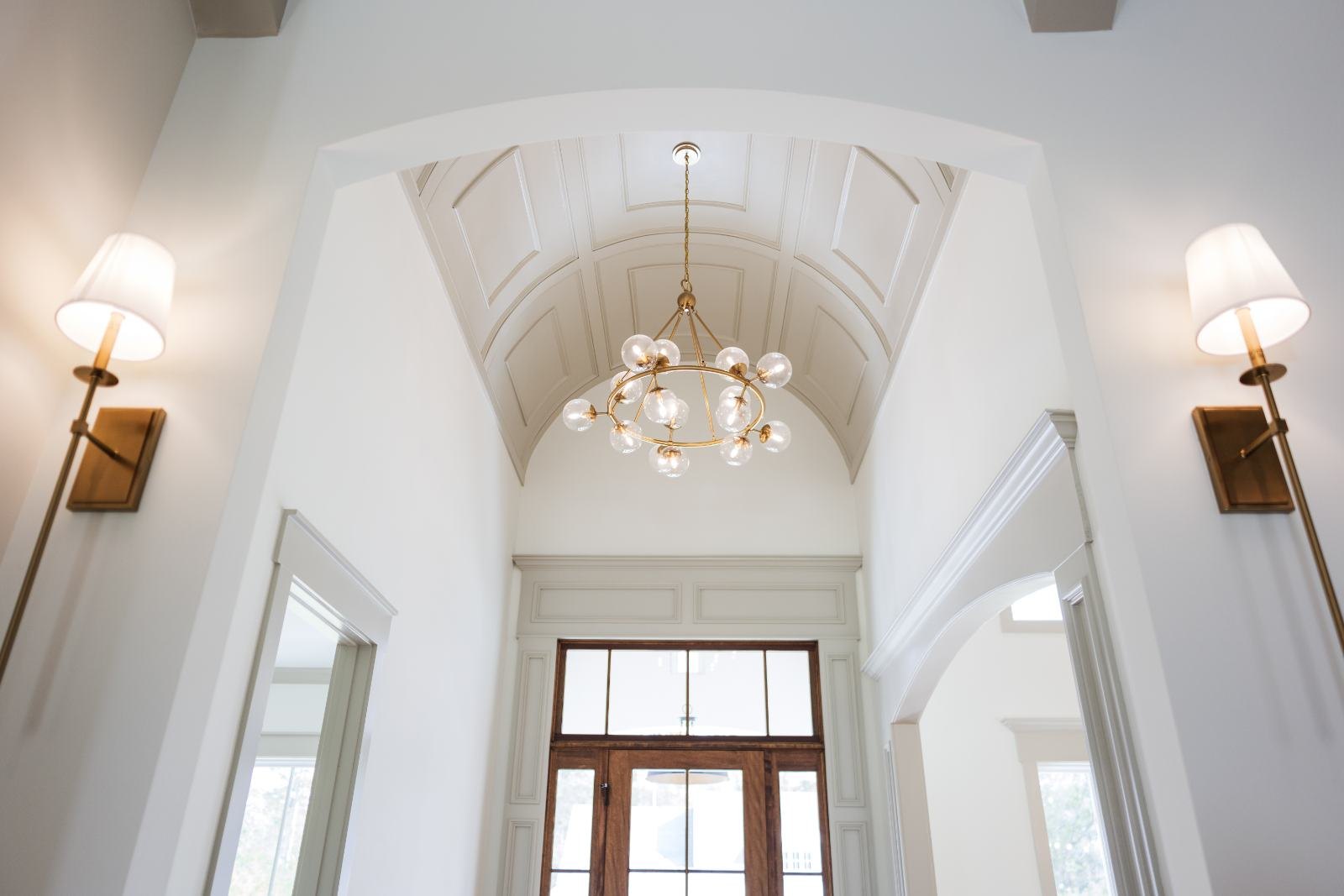 Two-story foyer with paneled walls, sconces and a barrel ceiling