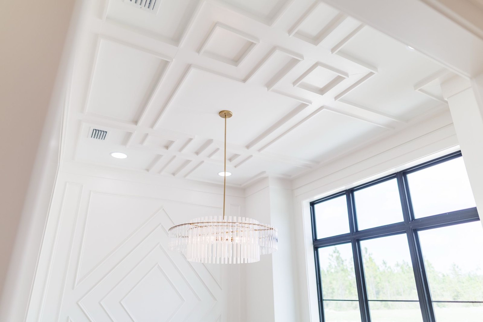 Dining room with a white waffle ceiling, diamond wall panels and a crystal chandelier