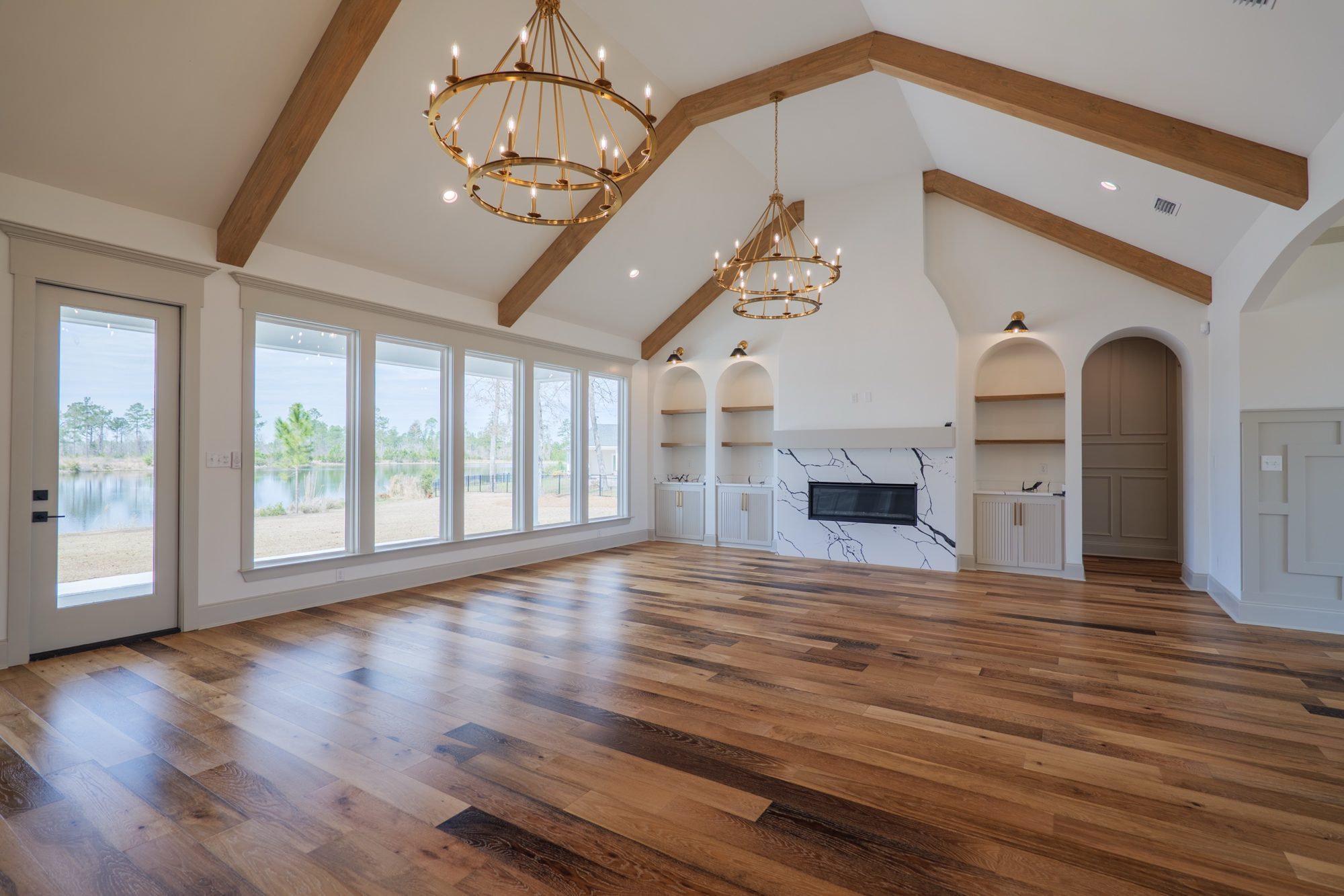 Great room with three brass chandeliers and a wall of windows on the lake