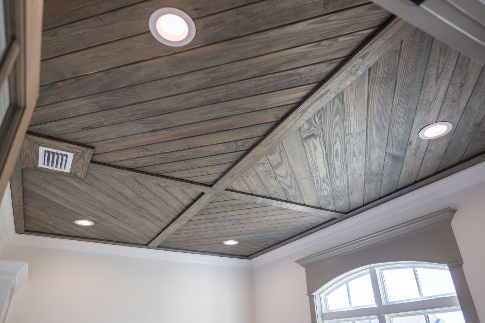 Room with a diagonal wood plank ceiling and an arched window