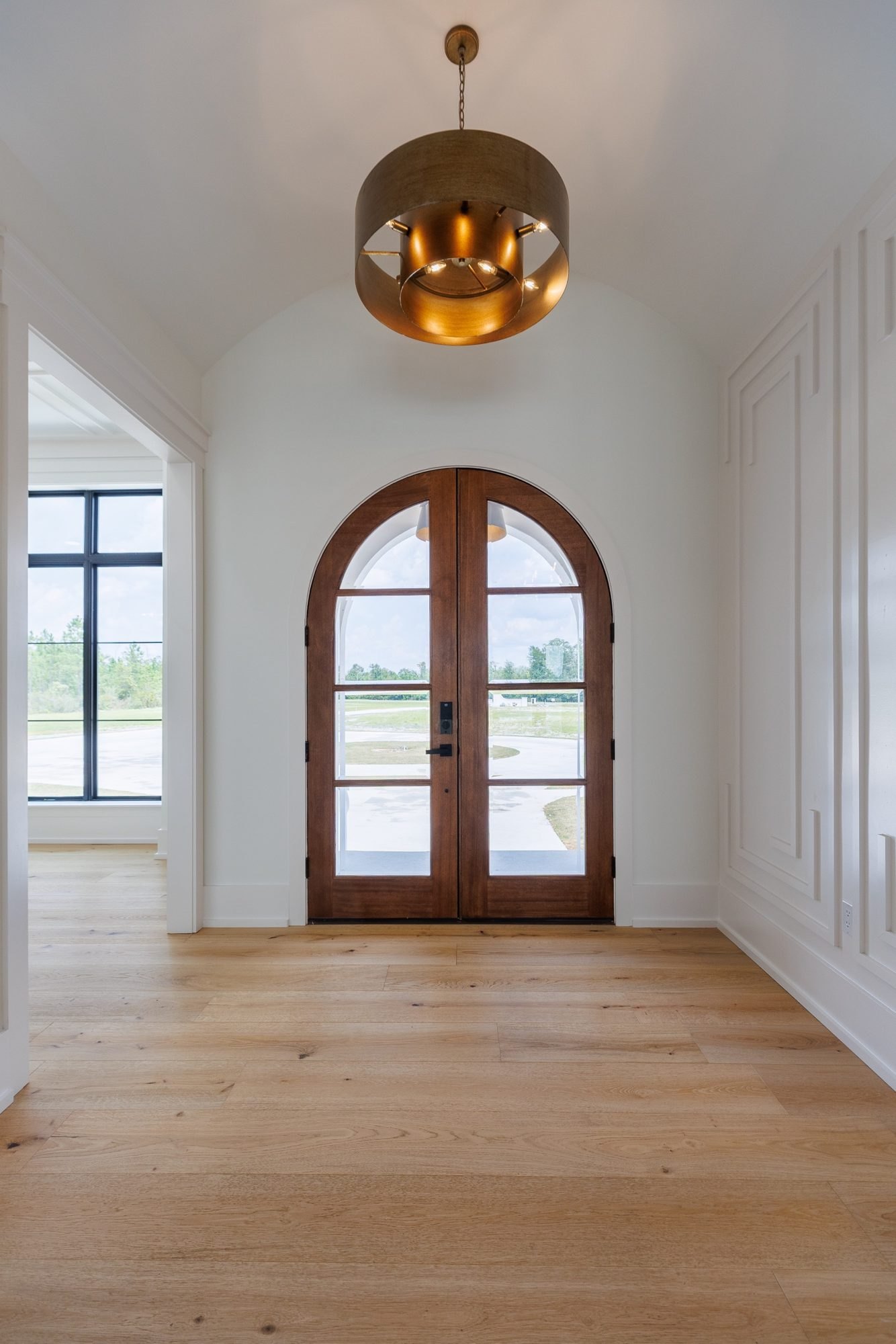 Arched wood front doors framed by paneled walls