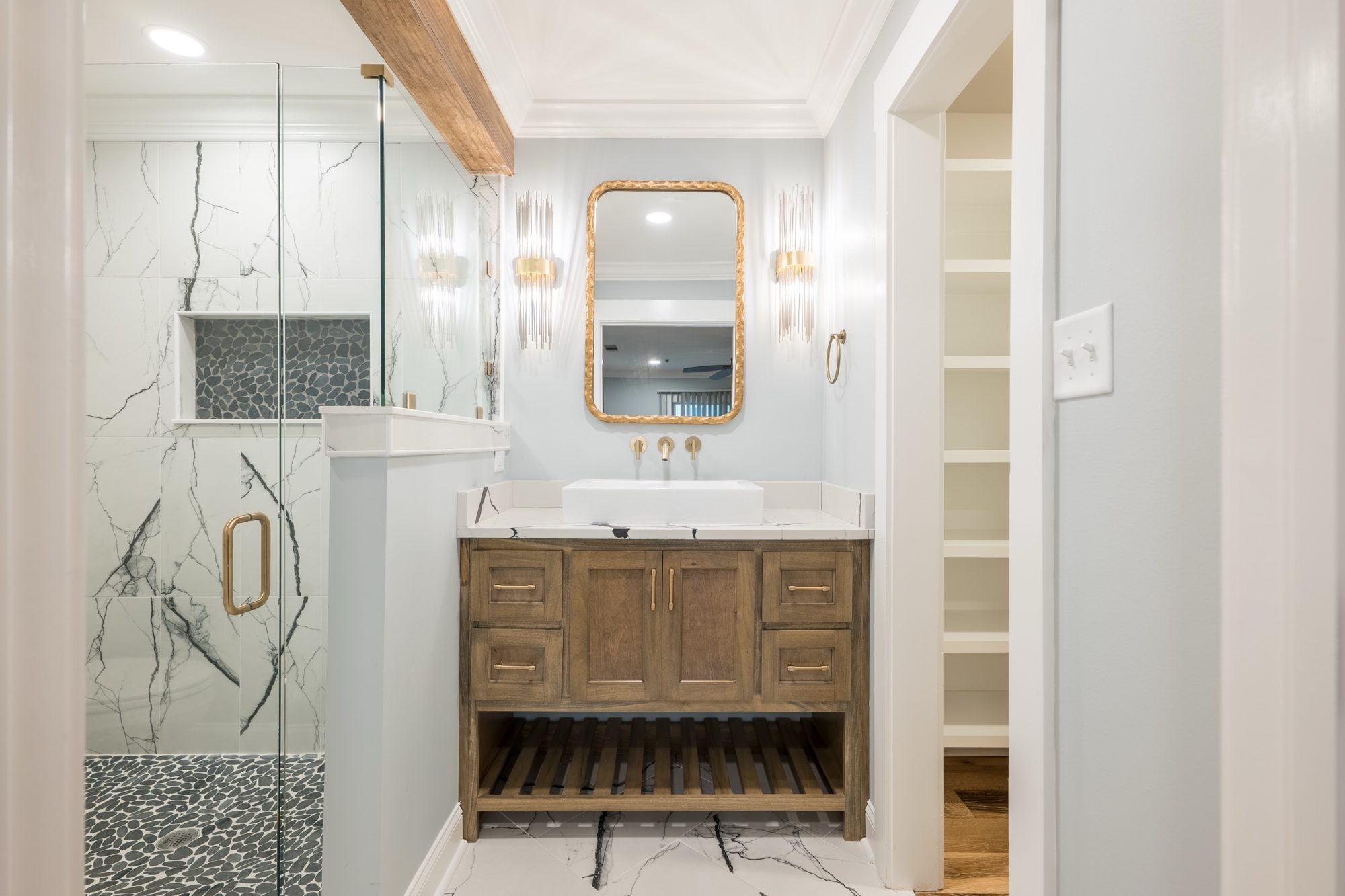 Renovated bath with a walnut vanity, gold mirror and marble-look tile