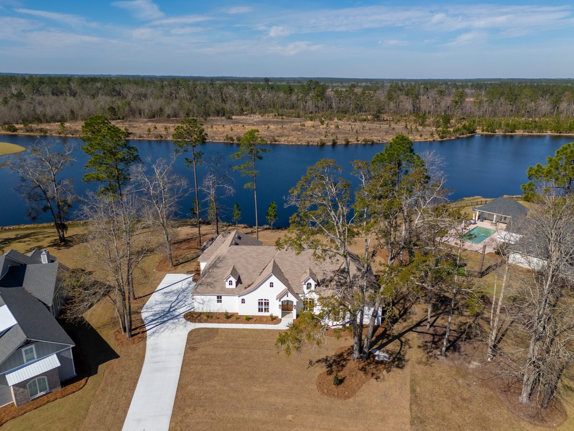 Aerial view of a white LaCatalina home on a wooded lakefront lot