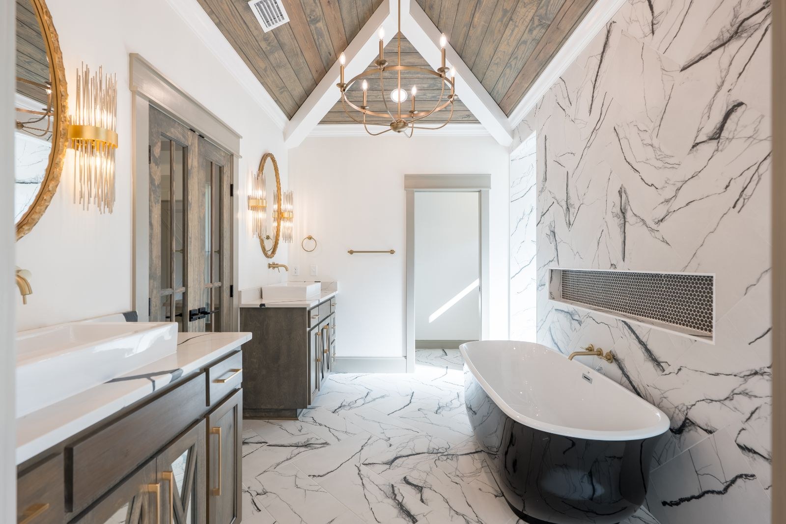 Primary bath with a vaulted wood ceiling, brass chandelier and black freestanding tub