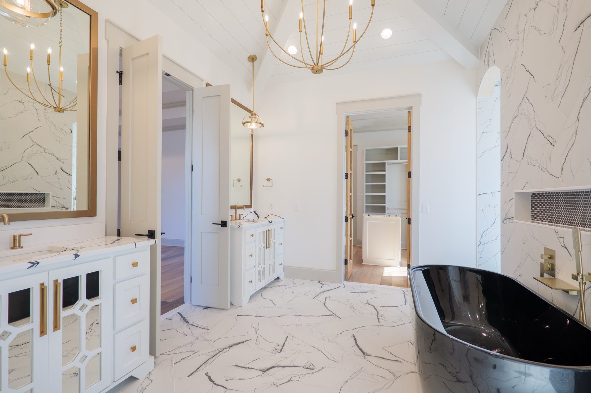 Primary bath with a black freestanding tub, marble tile and a brass chandelier