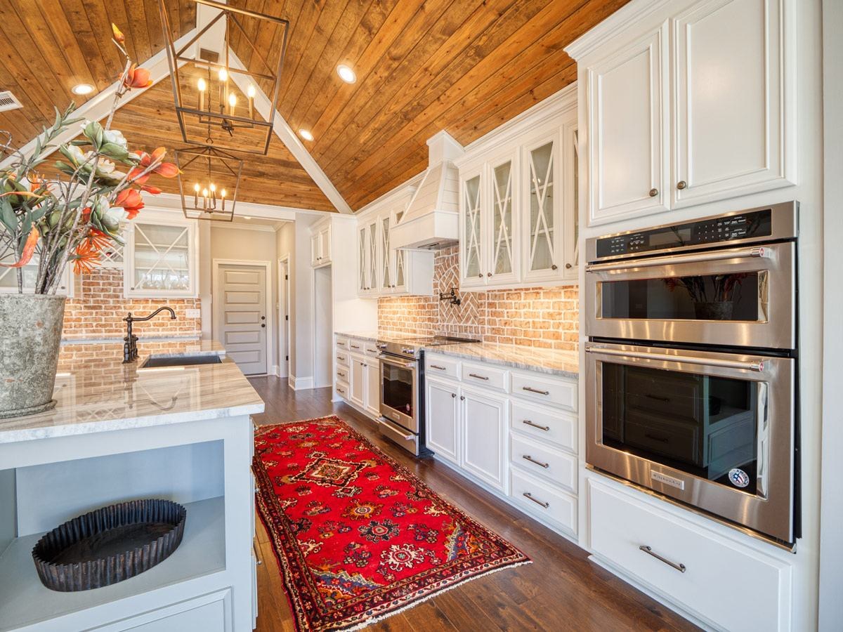 White kitchen with glass-front cabinets, brick backsplash and a red rug
