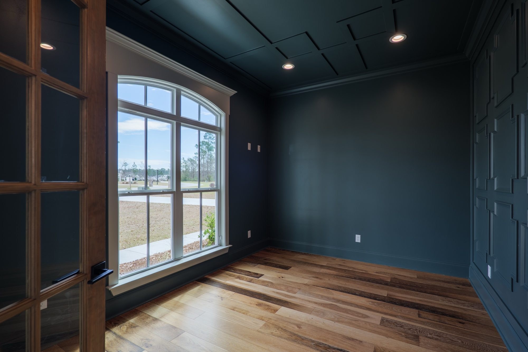 Home office with navy paneled walls, an arched window and glass French doors