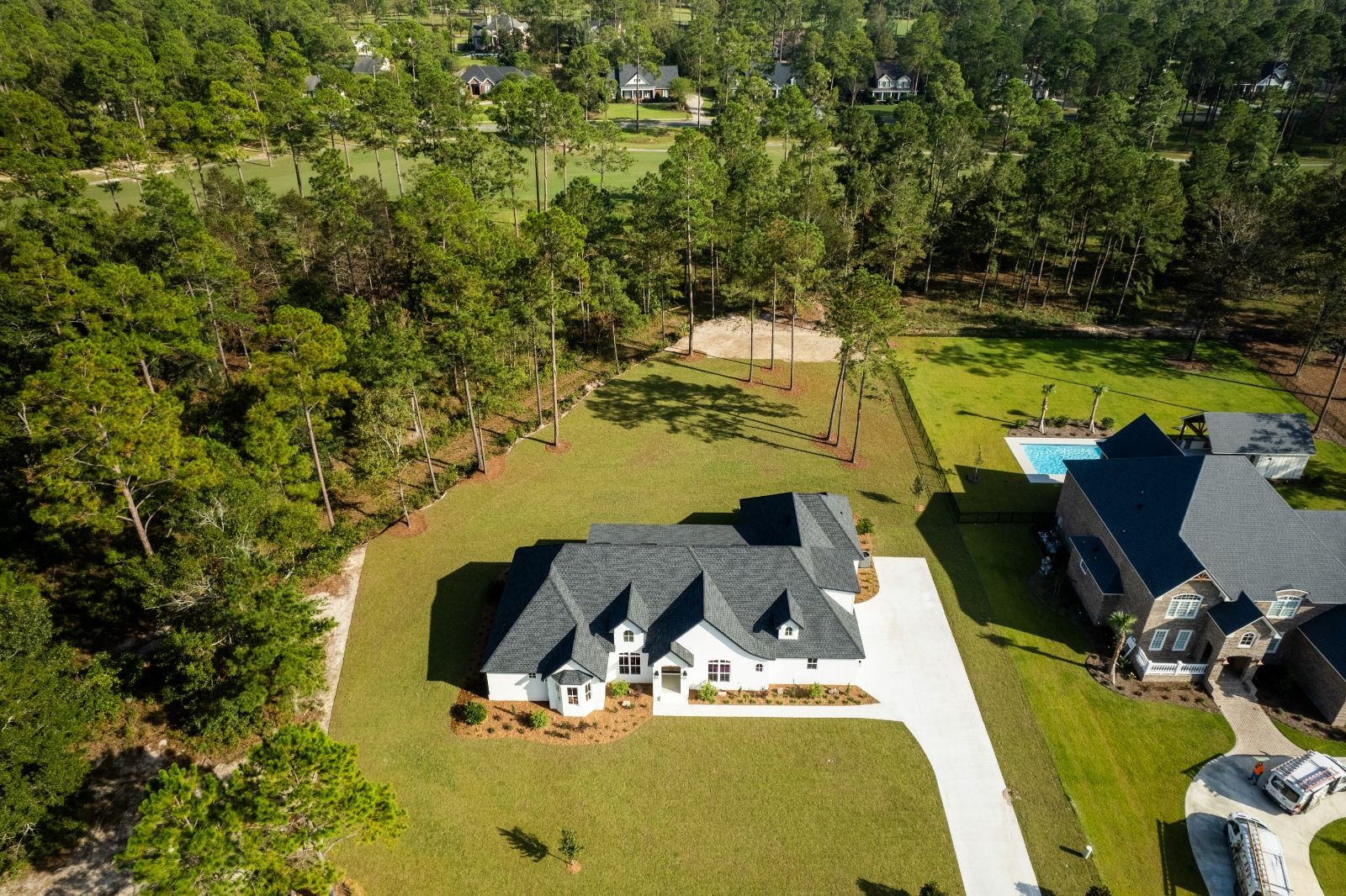 Bird's-eye view of a white LaCatalina home on a wooded lot with a long driveway