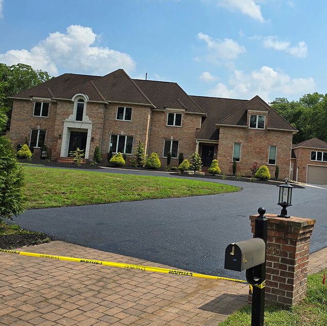 Freshly paved black asphalt driveway curving up to a large brick estate home in Gloucester County, NJ