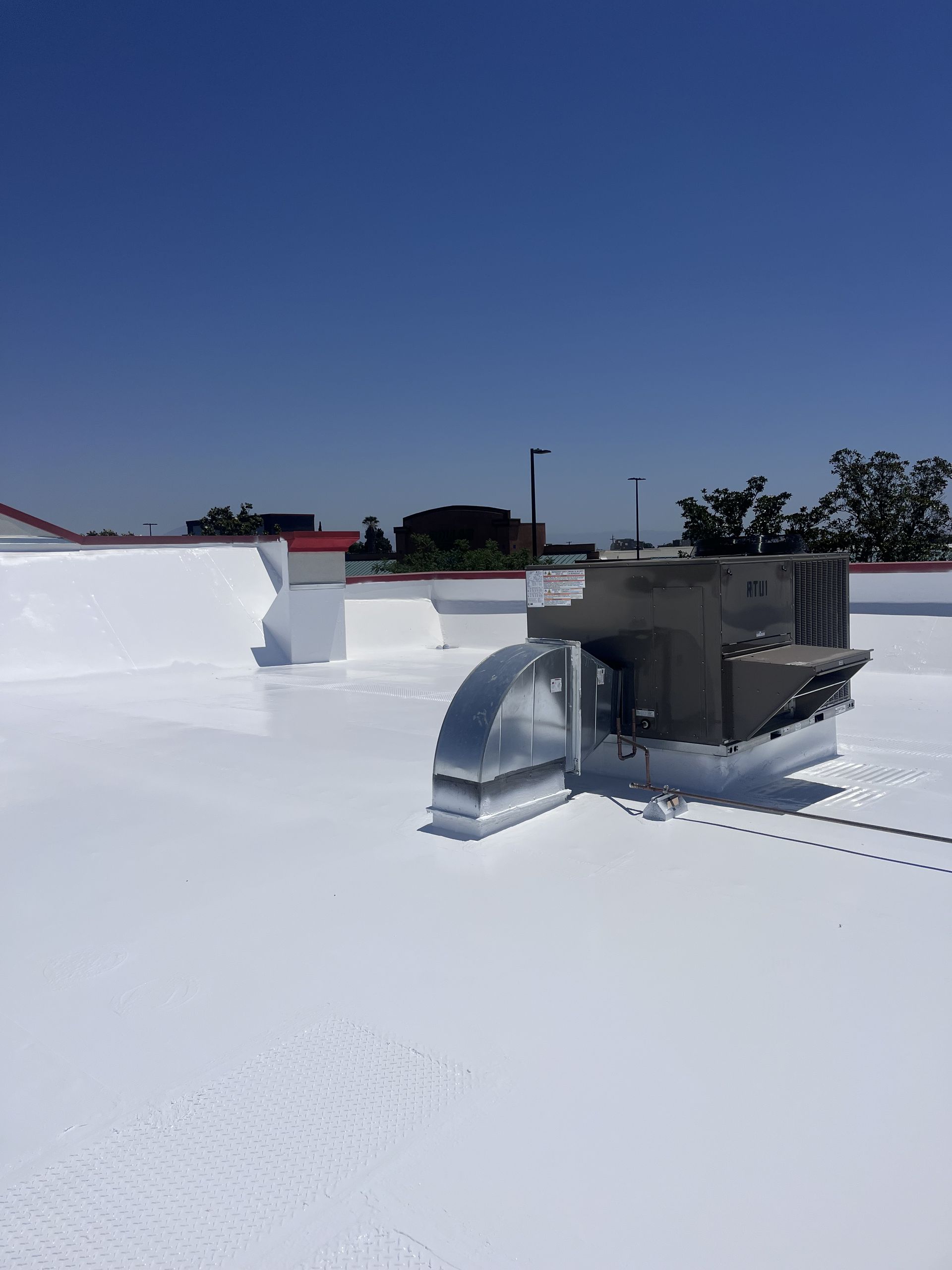 Bright white roof coating on a commercial flat roof around a rooftop HVAC unit