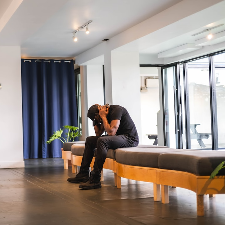 Man sitting in waiting room at medical office, frustrated with hands on back of nek