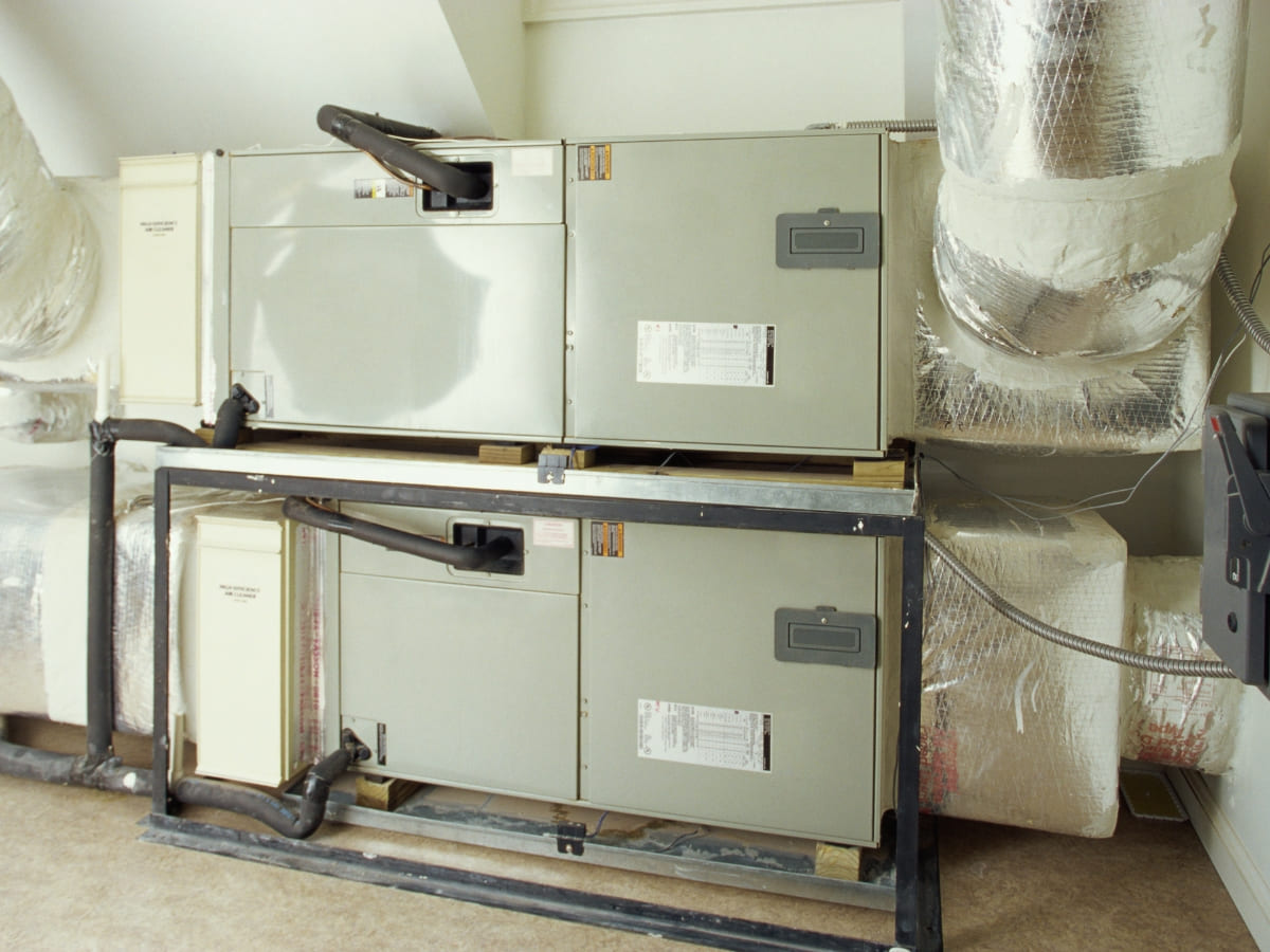 Two large HVAC units installed in an indoor mechanical room, with insulated ducts connected above.