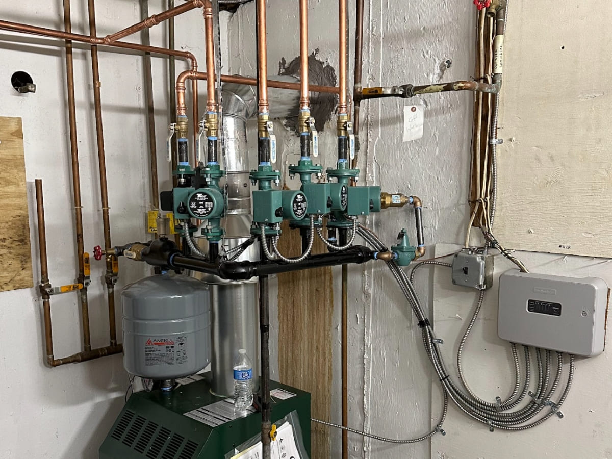 A neatly arranged set of plumbing and heating components, including a water heater, copper pipes, and circulating pumps, installed in a basement.