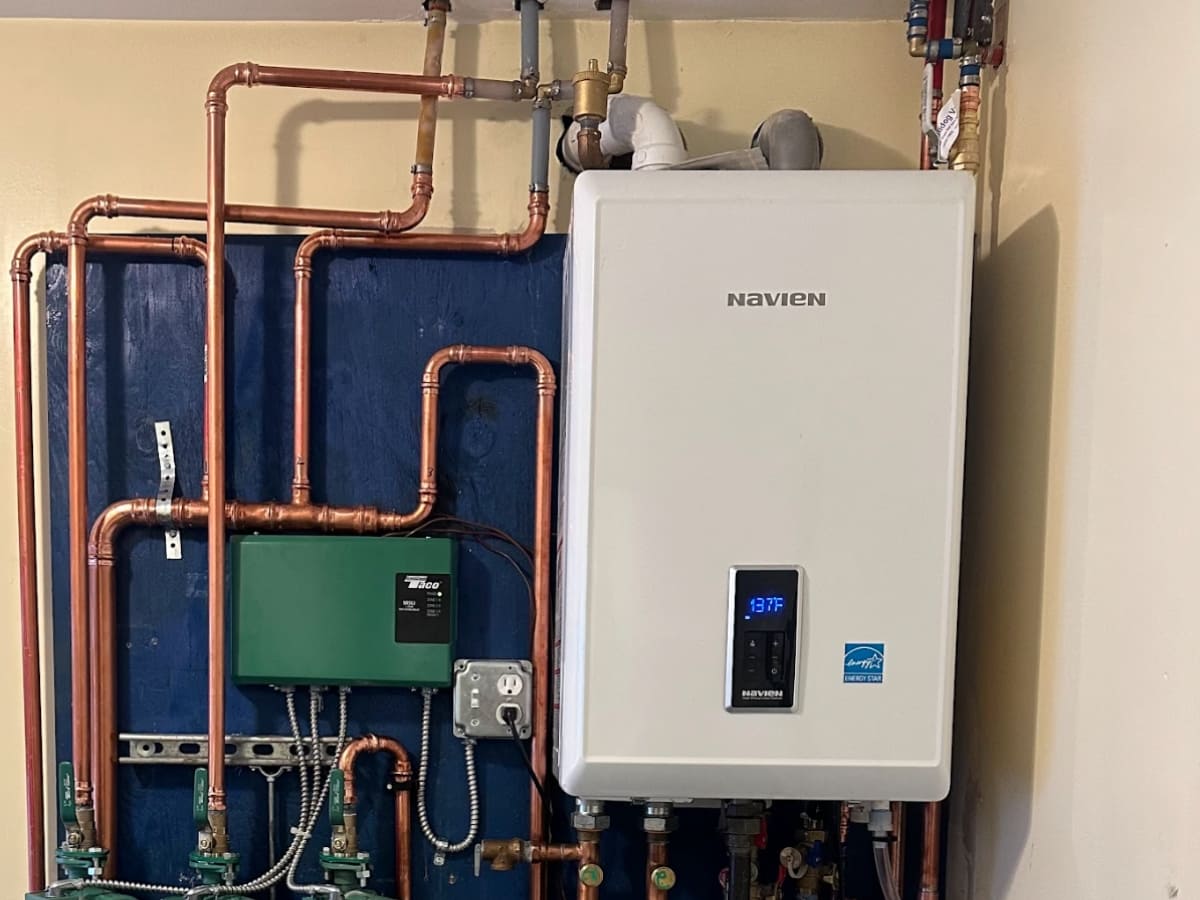 Modern boiler system installed on a blue wall, connected with copper pipes and a digital temperature display.