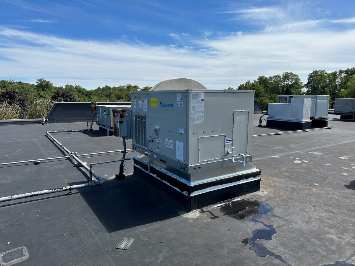 Commercial rooftop air conditioning unit on a flat roof with other HVAC equipment visible in the background