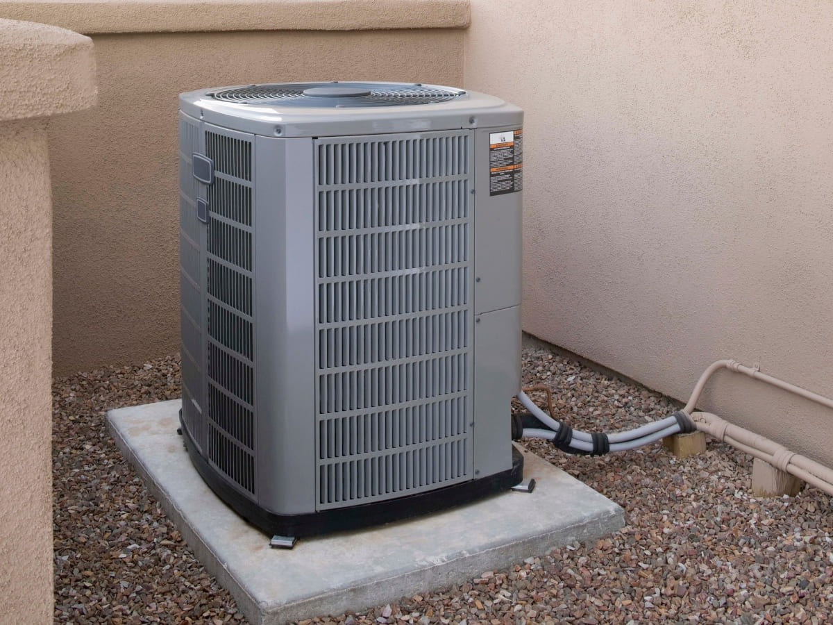 Outdoor air conditioning unit installed on a concrete slab next to a building with beige stucco walls